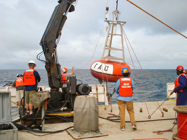 NOAA scientists and technicians on the deck of a ship preparing to deploy a TAO buoy, being held up by a crane