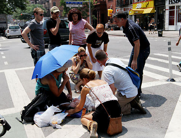 A group of people surround a woman lying on pavement