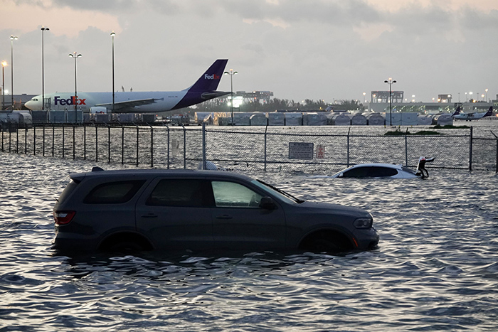 an SUV and a sedan parked in flood waters with an airplane parked on the tarmac in the background