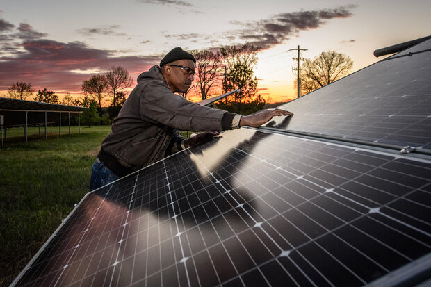 Man reaching arm across a ground-installed solar panel