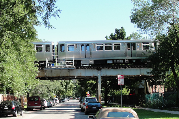 An elevated train crossing a tree-lined street