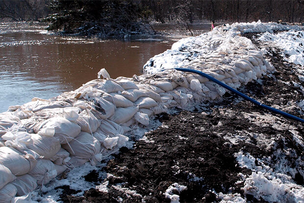 3-foot-high wall of sandbags with water on one side and mud on the other