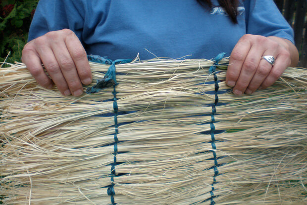 A woman holding a section of woven beargrass tied with blue ribbons