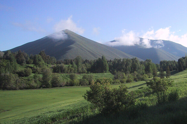 Blue sky, cloud-topped mountains, green trees