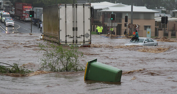 Flooded intersection with a woman sitting on top of a stranded car in the background