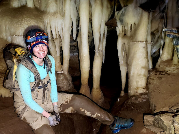 Babs sitting in front of stalactites and flowstone that look like tea-stained ivory