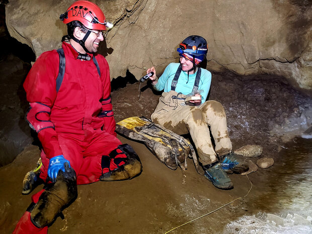 Two scientists wearing hard hats and hip waders sit in a cave