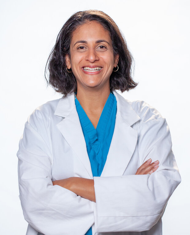 Dr. Patel in a white doctor's coat over blue scrubs