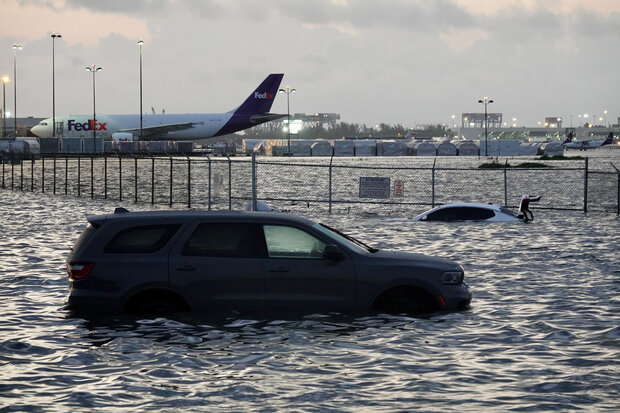 Photograph of a car flooded at an airport with a second vehicle and planes in the background in Florida.
