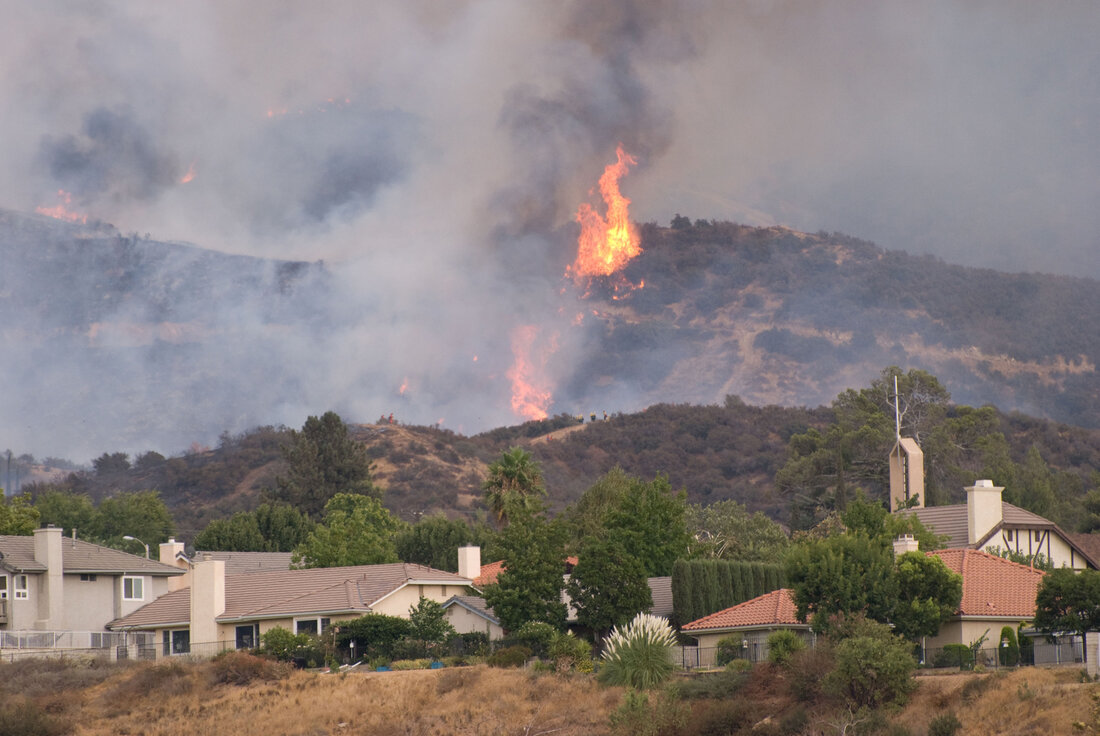 open flames burning on a vegetated hillside above a collection of houses