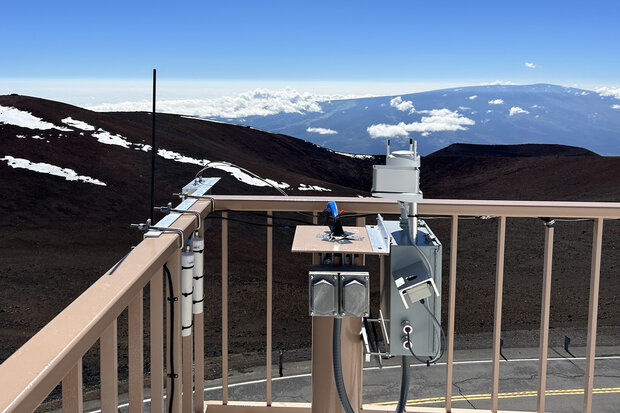 Air sampler attached to railing of deck overlooking snow-dotted mountains