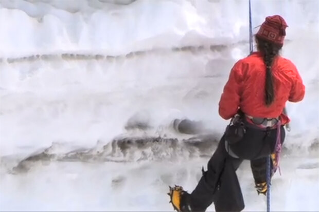 Photo of a scientist hanging from a rope into a snowpit that shows soot layers